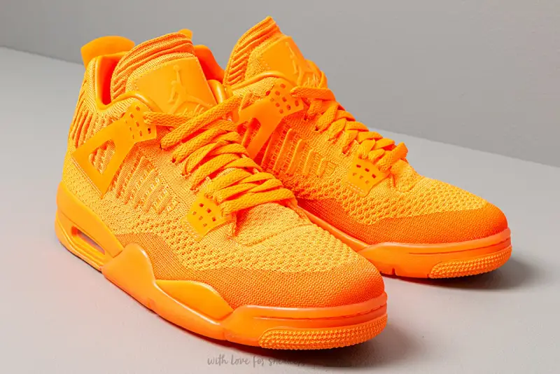 Un paio di scarpe Jordan 4 arancioni brillanti, con tomaia in maglia e dettagli iconici.